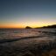 sunset shot of the sea with the shadow of a mountain at distance