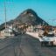 green mountain peak at the end of a roadwith a few cars at a distane and a three wheel vehicle that seems to be selling homemade produce driving around