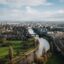 river runs through the city with plenty of houses and green fields near it under a cloudy sky