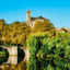 green trees and bushes and a concrete bridge over body of water under a clear blue sky