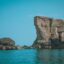 blue sky over the calm blue sea with some people preparing to jump off rocks to the water