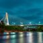 lighted bridge connecting two parts the city filled with green trees, above body of water