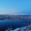 aerial view of snowed down city buildings and body of water under a clear blue sky in Tromso, Norway
