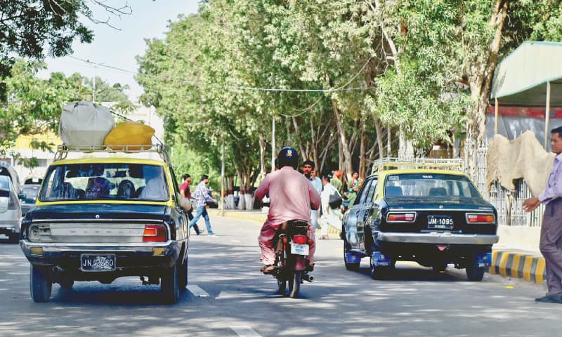 two black vehicles with a yellow roof and baggage racks on top in traffic