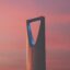 A tall ornamental cylindrical shaped building against a pink sunset sky.