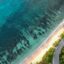 A bird's eye view of the ocean running parallel to a strip of sand next to a road and a forest.
