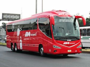 ADO Bus Cancun Airport A red ADO bus driving on the road, providing transportation from Cancun Airport, with large windows and luggage compartments visible.