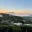 A view of Olbia's landscape from afar, showing houses and greenery with the sea and islands behind it and the sun setting in the distance