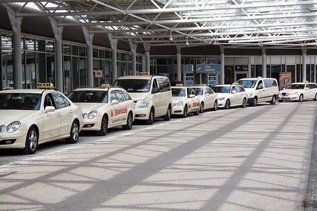 A line of beige Olbia airport taxis waiting outside the Departure Terminal, taxis in Italy can also be white.