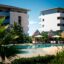 Tropical view of a luxury hotel resort with palm trees, a central swimming pool, and sun loungers at Atelier Playa Mujeres, showcasing the relaxing atmosphere awaiting travelers arriving from Cancun Airport to Atelier Playa Mujeres.