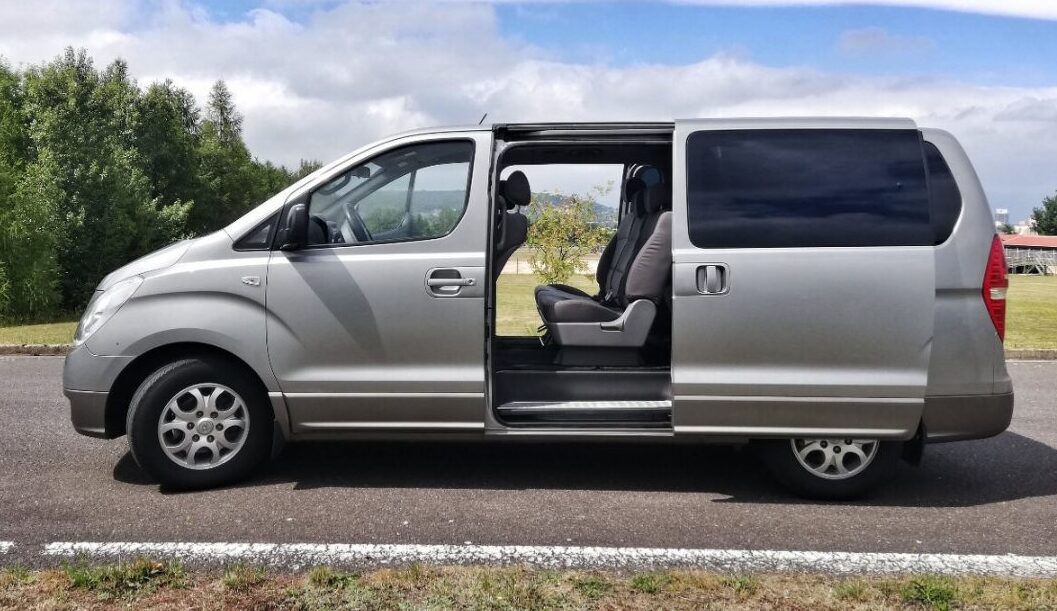 Side view of Prague Airport transfer vehicle on a road, a silver minivan with an open sliding door