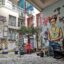 The courtyard of a hotel scattered with random chairs in different colors, a palm fern, and a mural with Frida Kahlo.
