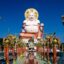 Front view of Big Buddha in Koh Samui, with a walkway lined with columns and intricate statues leading up to it and blue skies above.