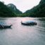 two wooden fishing boats floating on a wide river with mountains in the background