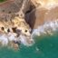Aerial view of turquoise waters lapping on a sandy shore with rocks.