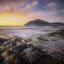 View of a beach and Almeria's coastline at sunset with clouds above and land separated by water in the distance.