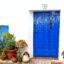A white house with a bright blue wooden door and potted plants on the left.