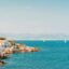 Turquoise waters with yachts on the horizon, blue skies above and the town of Antibes with rocks spilling into the sea.