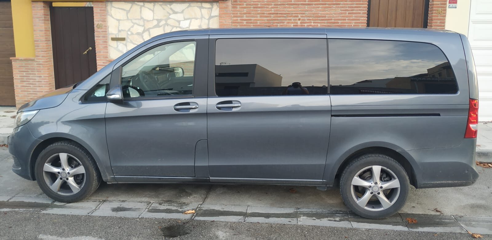 Side view of a silver/grey Granada Airport taxi (minivan) parked in front of a building.