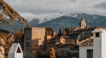 A view of the top of Granada's traditional buildings with mountains behind and clouds above.