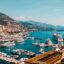 A view of Monaco's port with yachts in the marina and a view of the city and mountains behind.