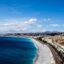 View of Nice beach and turquoise waters, with the city behind and blue skies above.