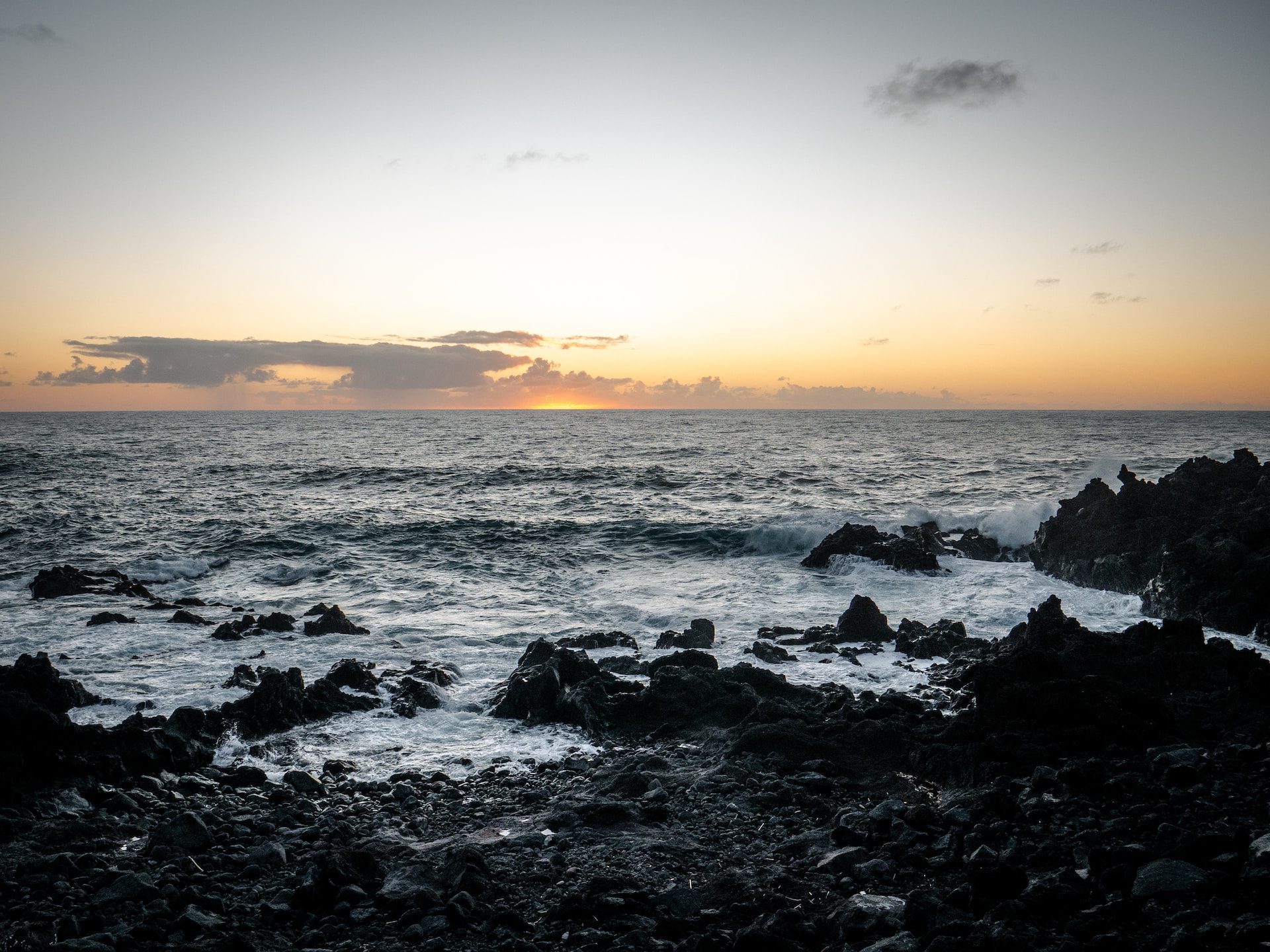 yellow and orange sunset over dark ocean waters and rocks