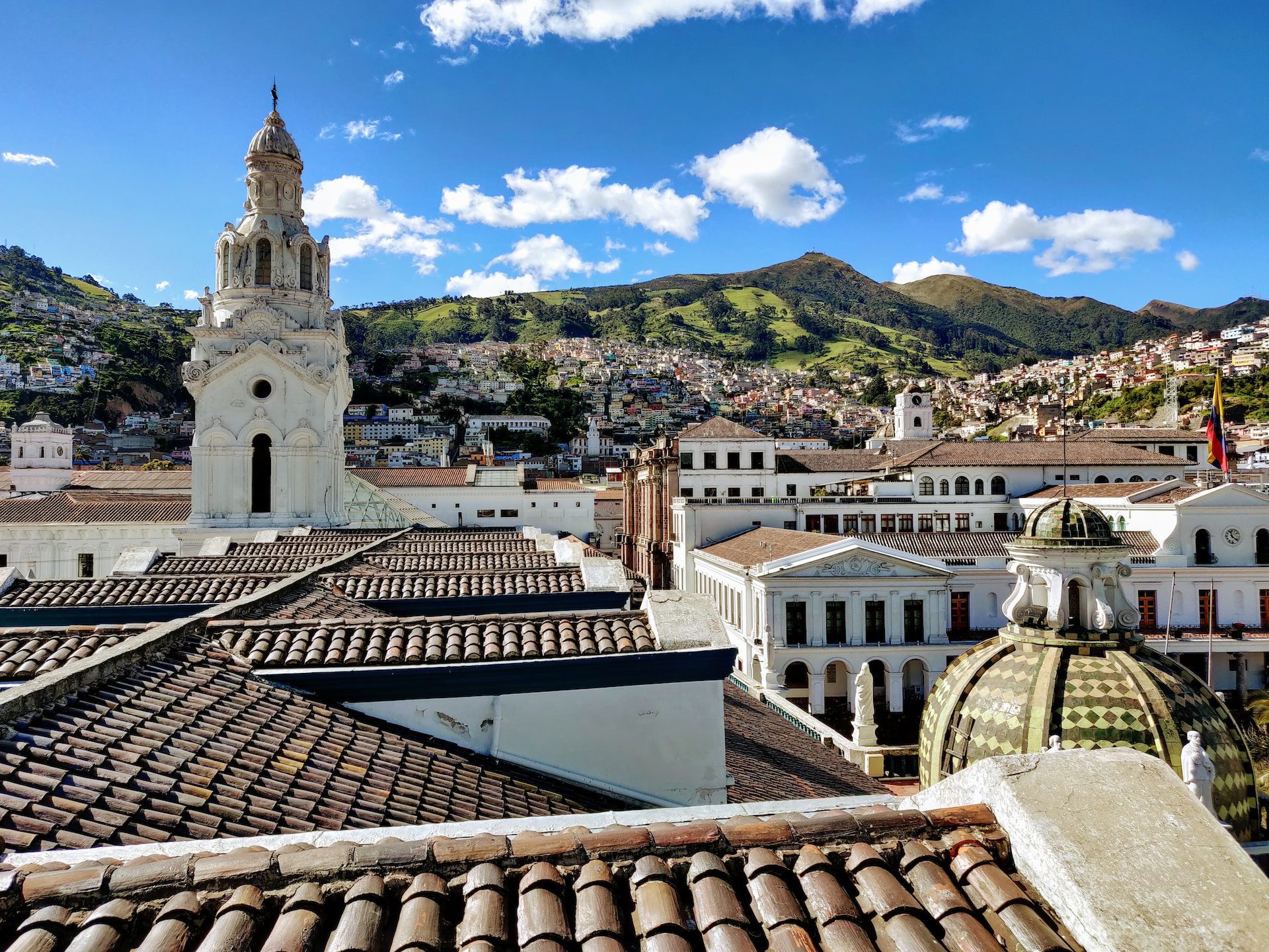 A view of the rooftops in the Old Town with a church tower and green hills in the background. Quito Airport departures