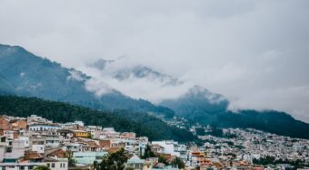 Colorful buildings scattered at the bottom of large mountains with clouds surrounding the peaks in Quito, Ecuador