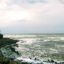 white rolling waves alongside palm tree lined cliffs under a cloudy sky