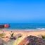 View of a white-sand beach in Candolim, with an old terracotta wall and lookout on the left side and blue skies above.