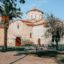 A quaint and pretty historic limestone church with a terracotta roof and a garden featuring palm trees.