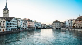 Heritage buildings in pastel colours of yellow, blue and white lining a waterway in Zurich city center.