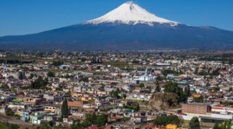 View of a snow-tipped mountain overlooking Puebla, with blue skies above.