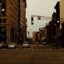 A group of cars stopped at a set of traffic lights on a city street surrounded by buildings.