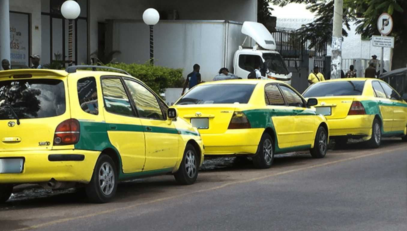 Yellow taxis with a green stripe lined up outside of a building.