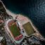 Aerial view of two sports fields within a city located on the edge of a body of water.