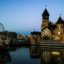 A ferris wheel and a castle with turrets lit up at night along a waterfront.