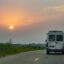 The tail view of a white van driving along a road towards the sun setting