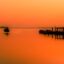 An orange sunset reflected on a calm lake with some wooden fishing boats