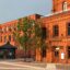 A large rectangular red-brick building with a single tree out the front of it.