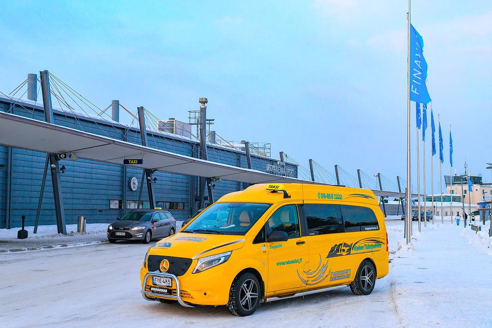 A yellow Rovaniemi taxi van outside the airport with snow covering the road.