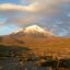 Countryside spanning toward snow-peaked a mountain under a cloudy bright sky.