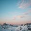 Expansive blue and orange sky with scattered clouds over snow ridden mountains.