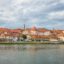 Red roofed buildings line the waterway in Maribor, Slovenia under a cloudy sky.