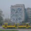 Three yellow trams parked in front of a white concrete building on a foggy morning, with blue graffiti-style art featured on the main face of the building.