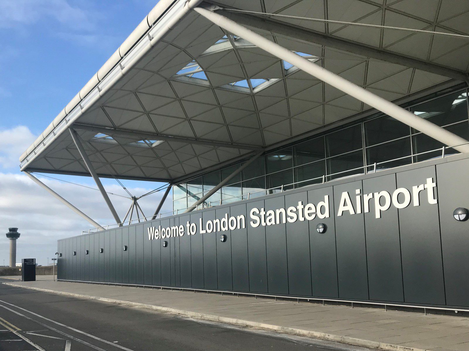 Exterior of Stansted Airport terminal building, with blue skies above and a "Welcome to Stansted Airport" sign on the side of the building.