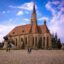Stunning building arcitecture and people walking in a plaza in Cluj, Romania under a cloudy blue sky.