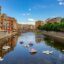 Buildings and blue sky reflect off a waterway in Girona, Spain.