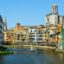 Colorful buildings closely line both sides of a waterway in Girona, Spain.